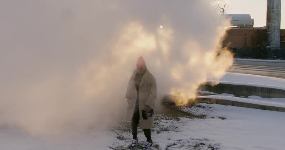 A man dances in steam by the street