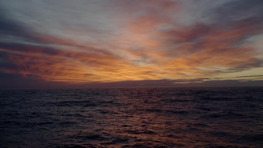 Rough waters in an ocean sits under a vibrant orange sunset