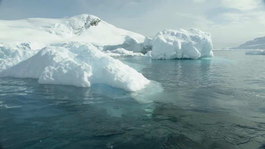 Smooth calm water flows around iceberg and snow