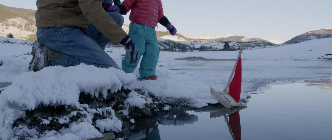 A young girl plays with a wooden boat in the snow and water