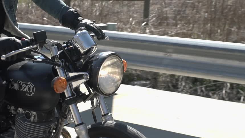 A person drives a motorcycle past a guardrail