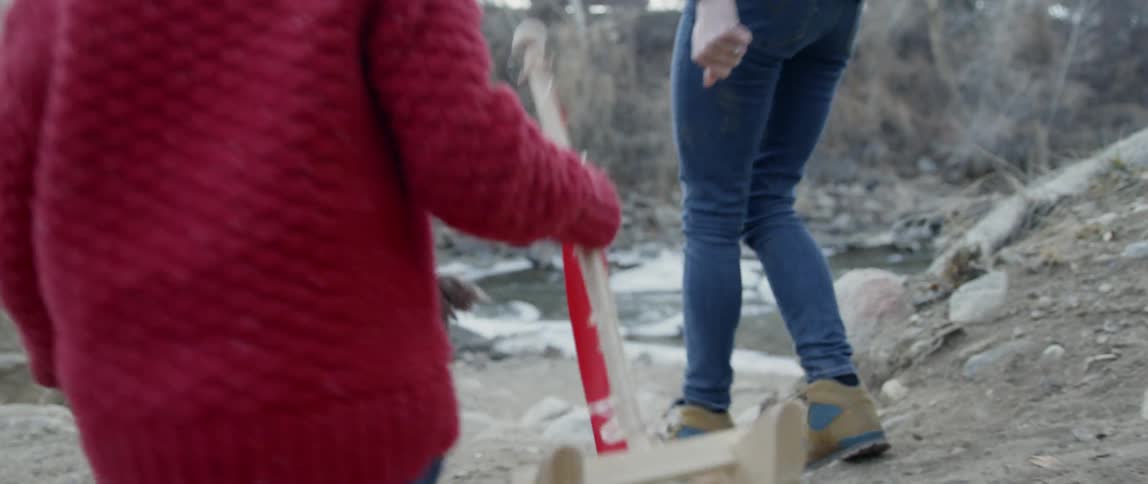 Young child carries a toy boat as he walks with a woman near a creek