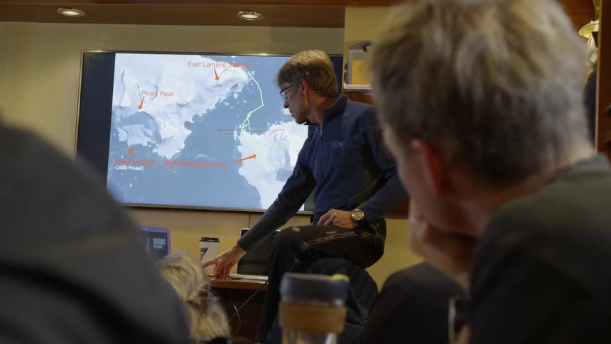 A man presents expedition information on slide in front of a class