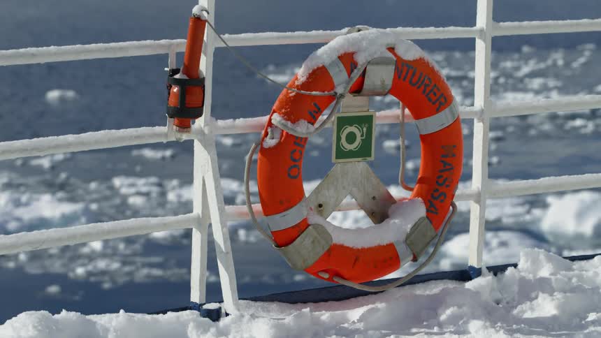 A life preserver is tied to the railing of a snowy ship