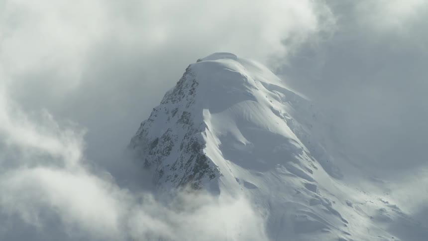 Clouds float around a snowy mountain peak