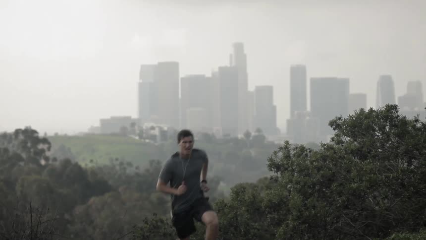 A man jogs up a hill with a city skyline behind him