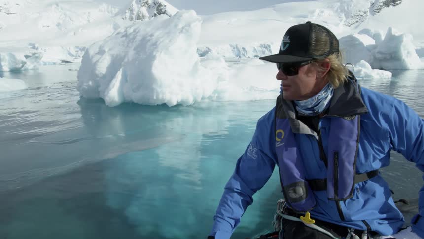 A man on a boat passes iceberg in clear water
