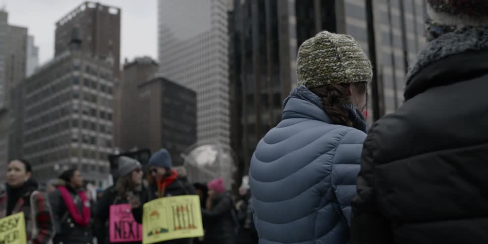 Protesters holding signs are marching down a city street in winter
