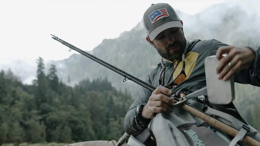 A fisherman is putting a container into his backpack outside during the day