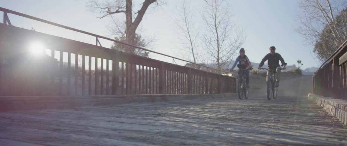Two bicyclists ride over a rural bridge at sunset