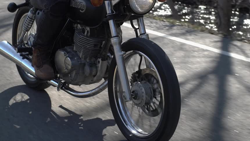 A person is riding a motorcycle on a road near a stream in daylight