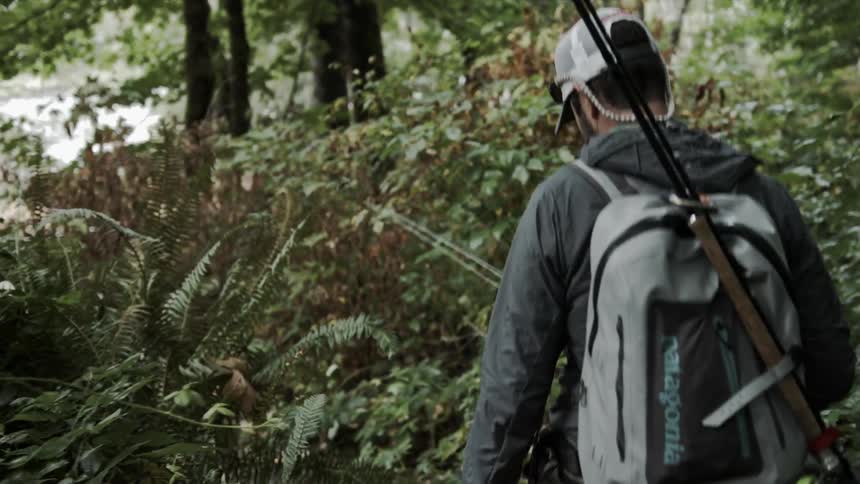 A man walks through the brush carrying fishing rods