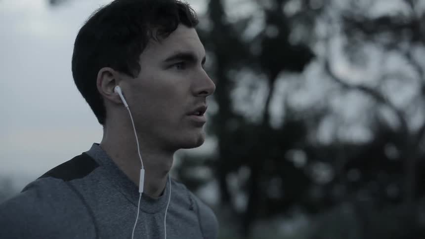 A man with earbuds in stands outside near trees