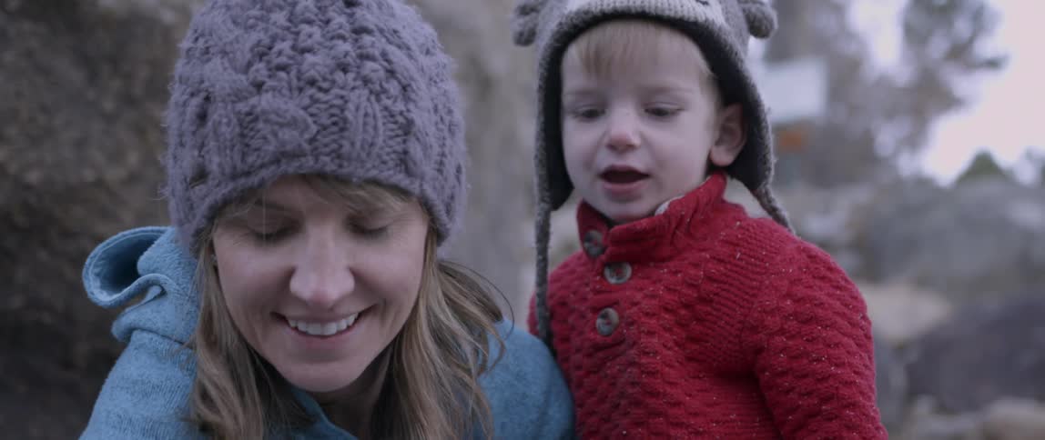 Woman holding small child smiles and waves outside on a cold day