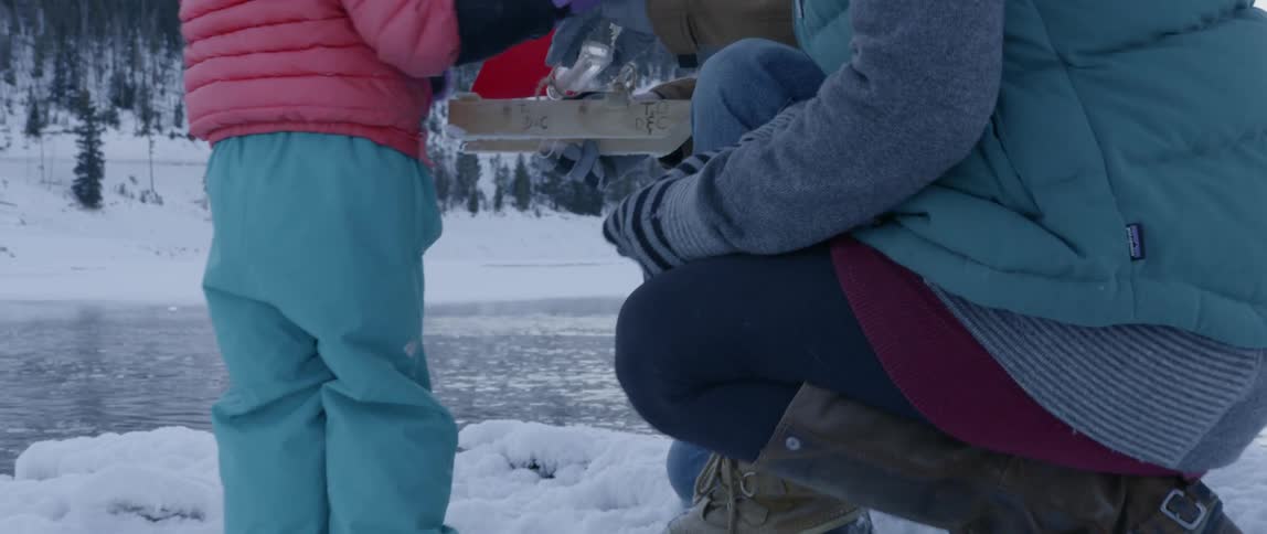 A young family holds a toy boat next to an icy river