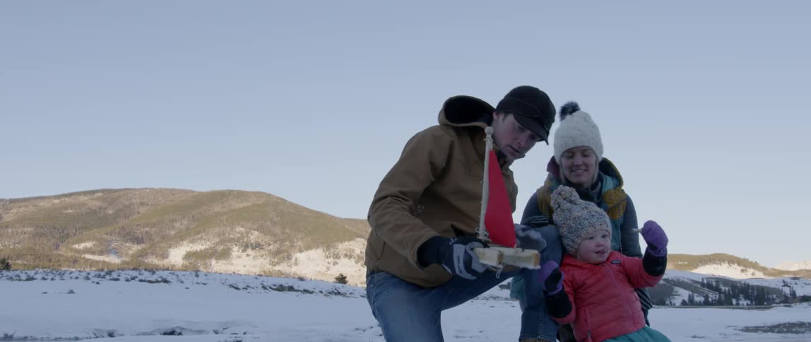 A young family holds a toy boat in the snow