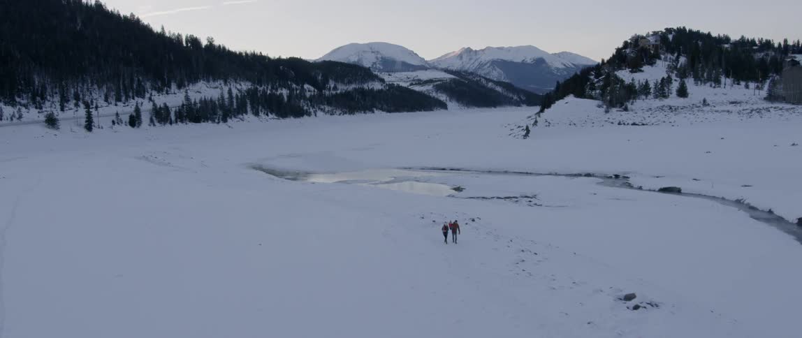 Two people are walking near a river in a natural setting in winter