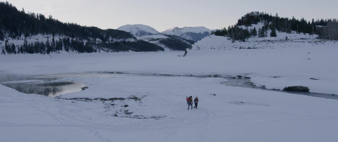People walk across a snowy landscape at sunset