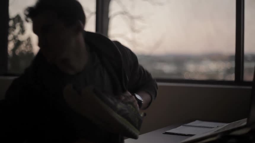 A man stands up from a desk at sunset