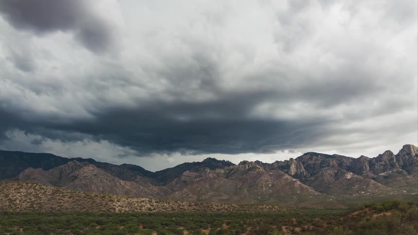 Lighting strikes as dark clouds fill the sky over a mountain range