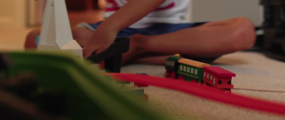 A boy plays with toy trains and cars on the floor
