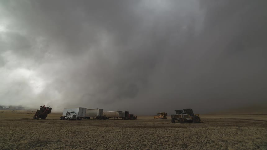 Timelapse of churning storm clouds over a field on a farm with parked trailers and equipment