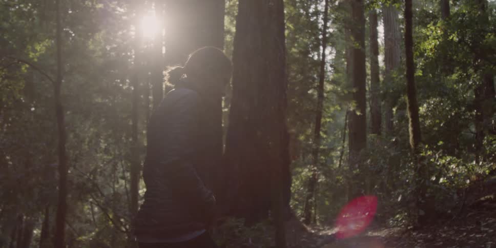 A woman walks in the woods in her hands in her pockets