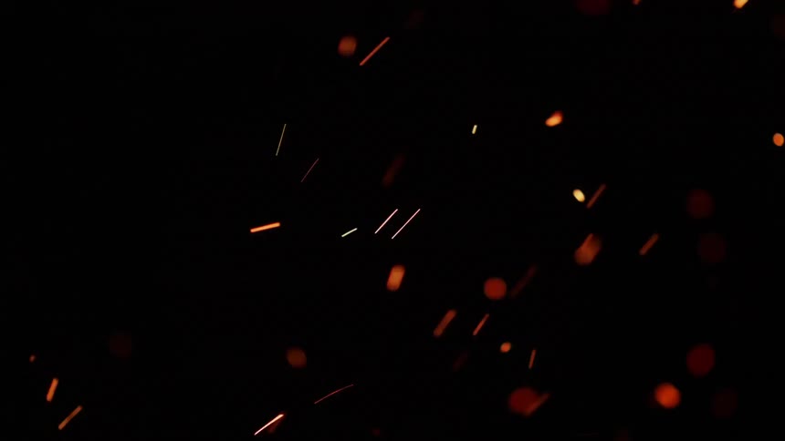 Sparks from a fire are flying into the air at night