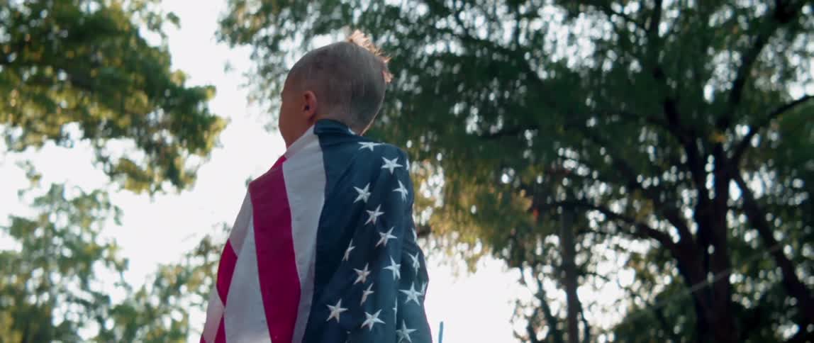 A young boy stands outside wrapped in an american flag
