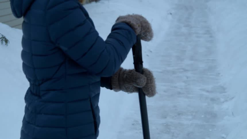 Person standing in the snow with a shovel at the end of a freshly shoveled sidewalk