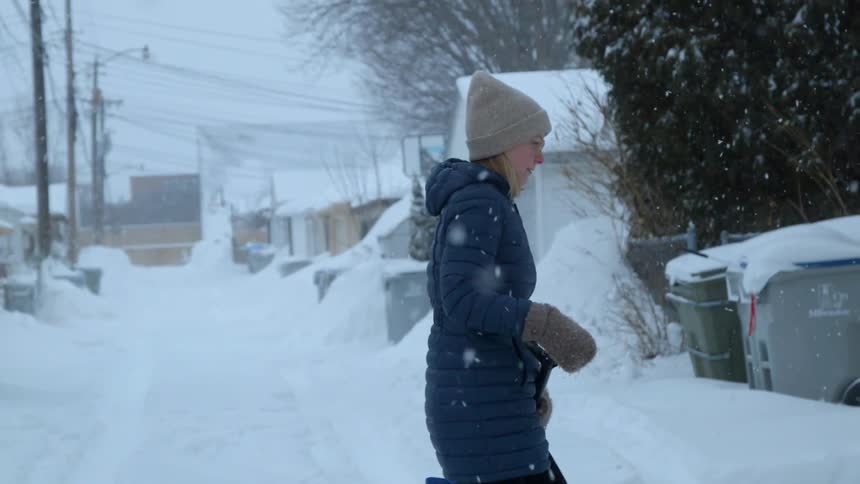Woman wearing a toque walks through the snow carrying a shovel