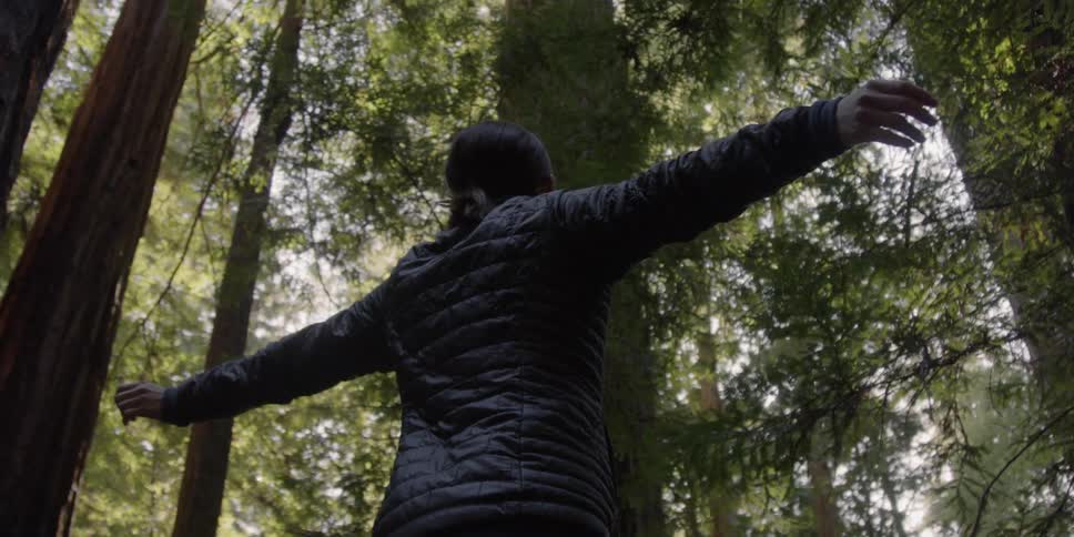 A woman holds her arms out in a forest