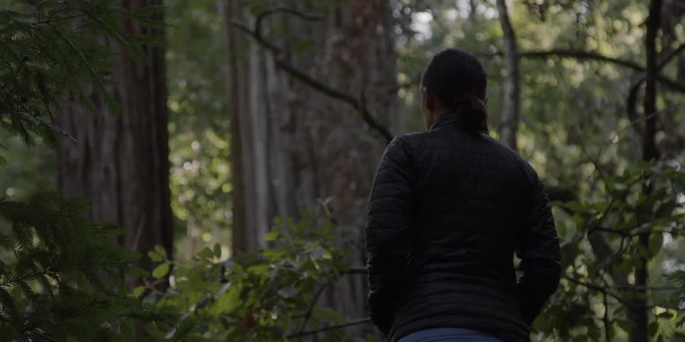 A woman stands and looks around in the forest