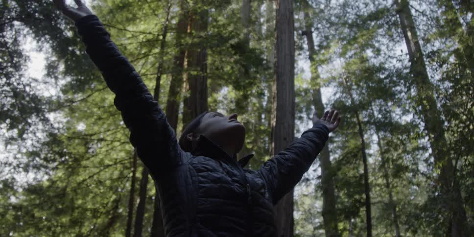 A woman spins around with her arms outstretched in a forest