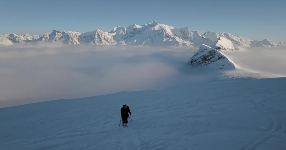 Two people hike uphill in the snow on a sunny day