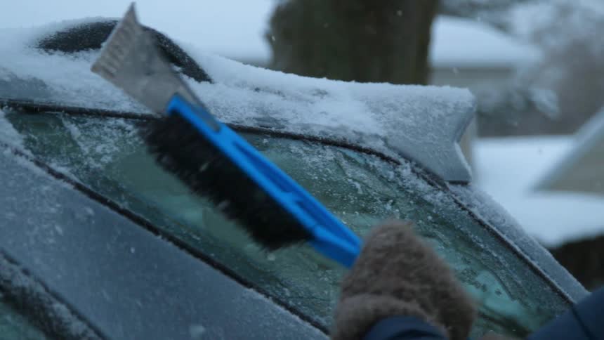 A woman scrapes ice from a car window