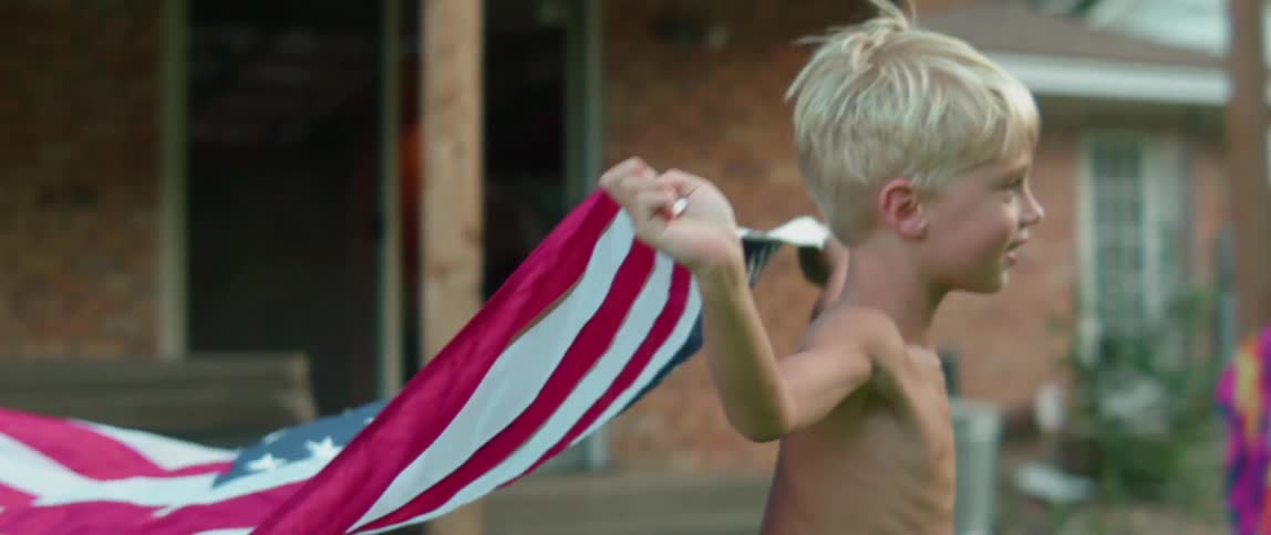 A young boy runs in a backyard while holding an american flag