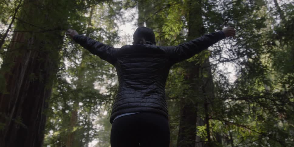 A woman spreads her arms and spins in the forest