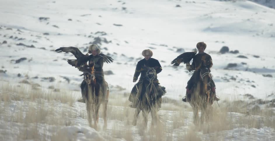 Men ride horses with hunting eagles in the snow