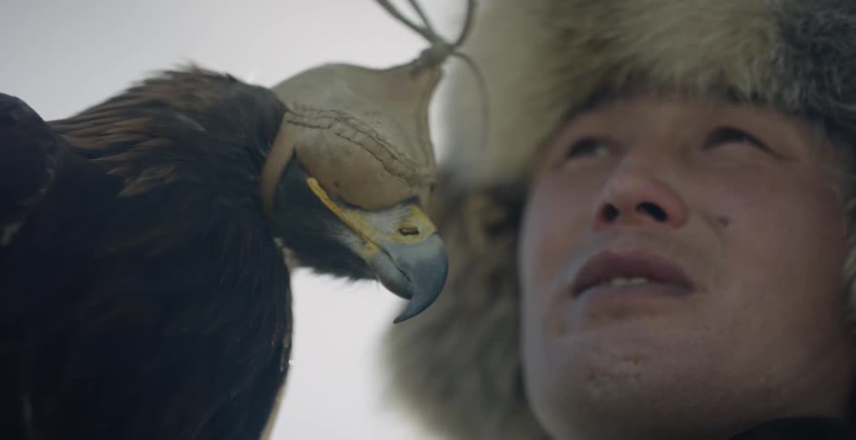 A mongolian man is holding a hooded hunting eagle
