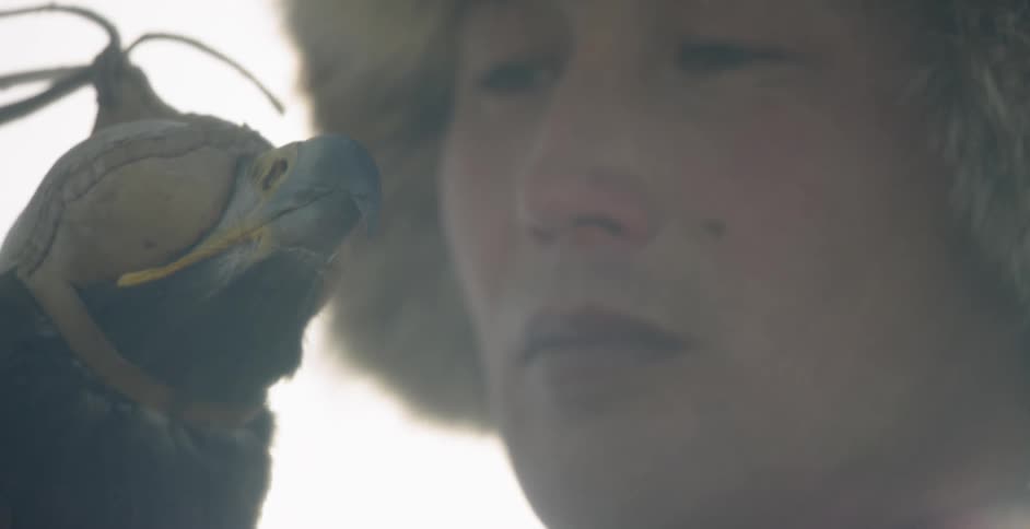 A mongolian man is holding an eagle outside in daylight