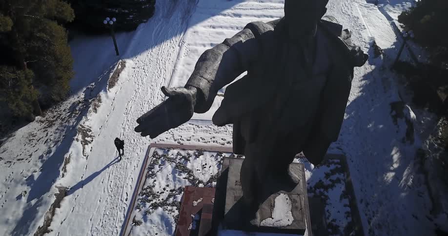 Person walks on a snowy sidewalk past a tall statue