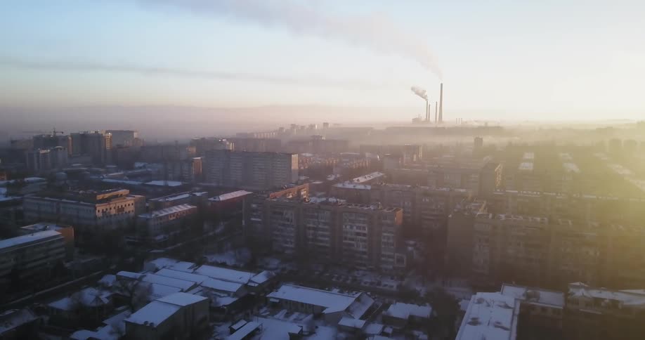 Large city near sunset with a large factory in the distance with smoke rising from its stacks