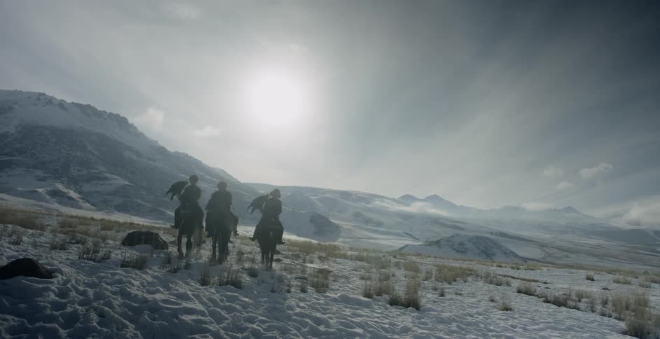 Men riding horses and holding large birds near sunset on a cloudy day