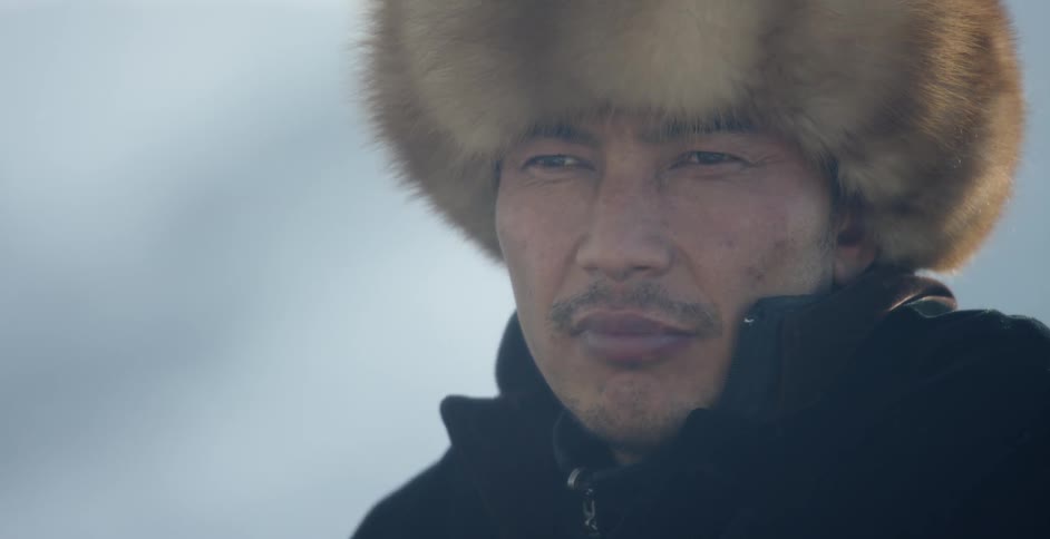 A man wearing a fur hat stares forward