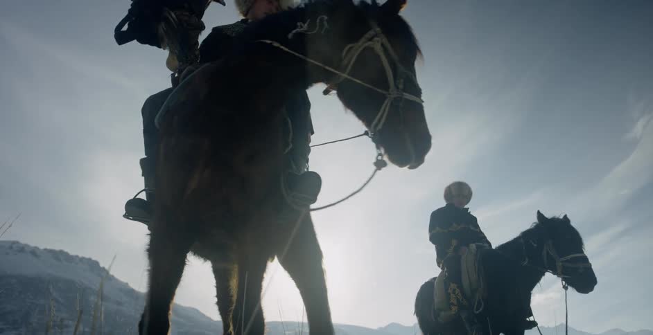 Two men ride horses near snowy mountains