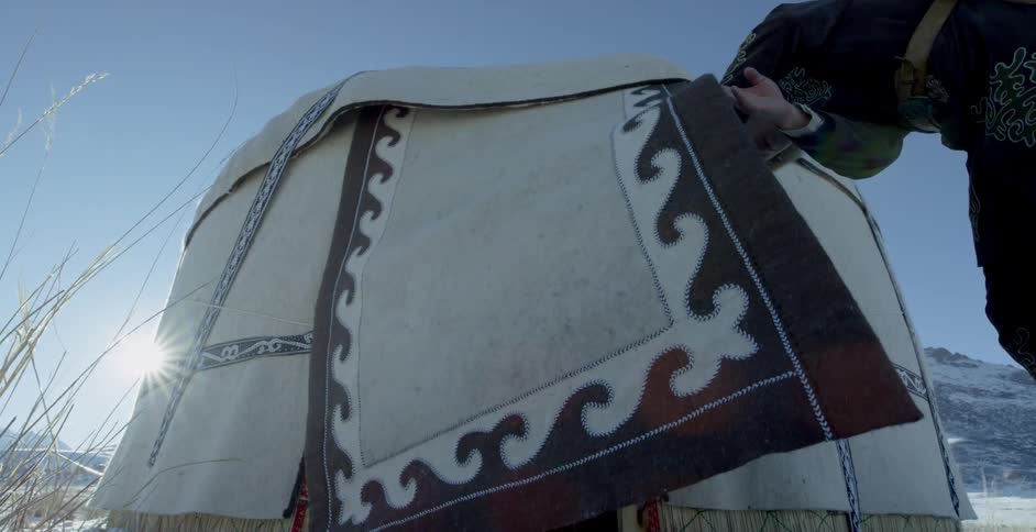 A man enters a yurt near snowy mountains