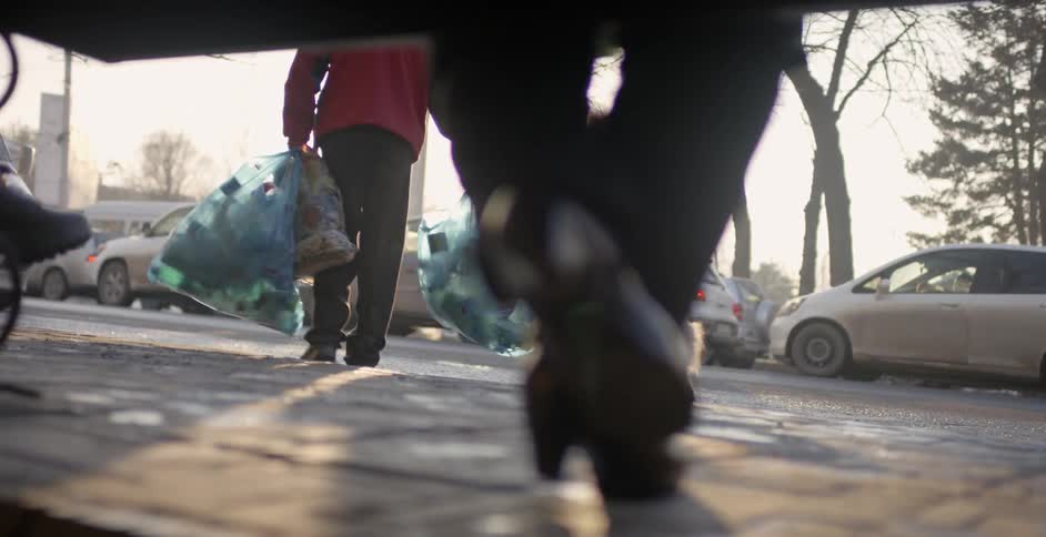 A dog follows a man carrying trash bags on a city sidewalk