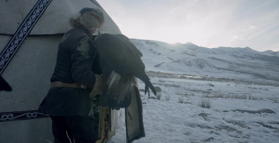 A man holding a large bird enters a yurt