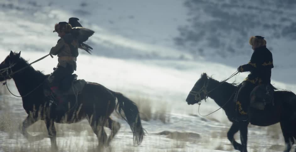 Men ride horses with a hunting eagle in the snow